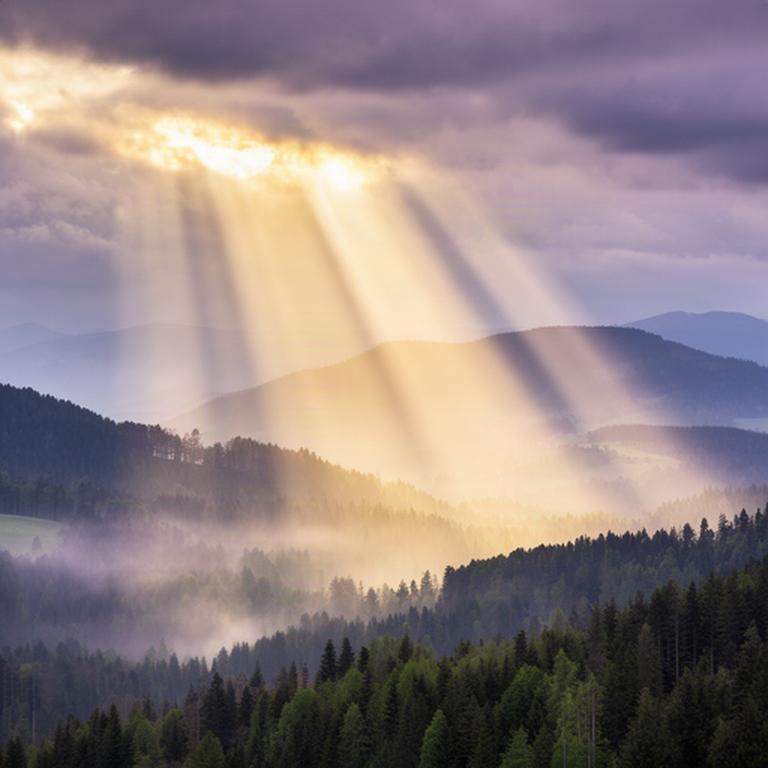 Sonnenstrahlen fallen durch aufreißende Wolken auf die bewaldeten Hügel der Steiermark